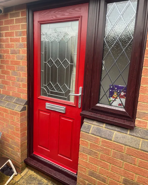 Red composite back door with patterned glazed panel and white uPVC frame.