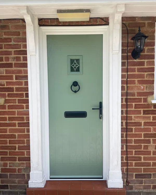 Traditional style pale green composite front door with square glazed panel at top.