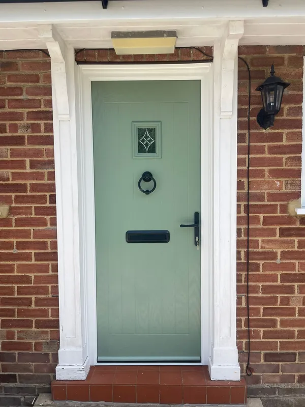 Light green composite front door with small square decorative glass panel.