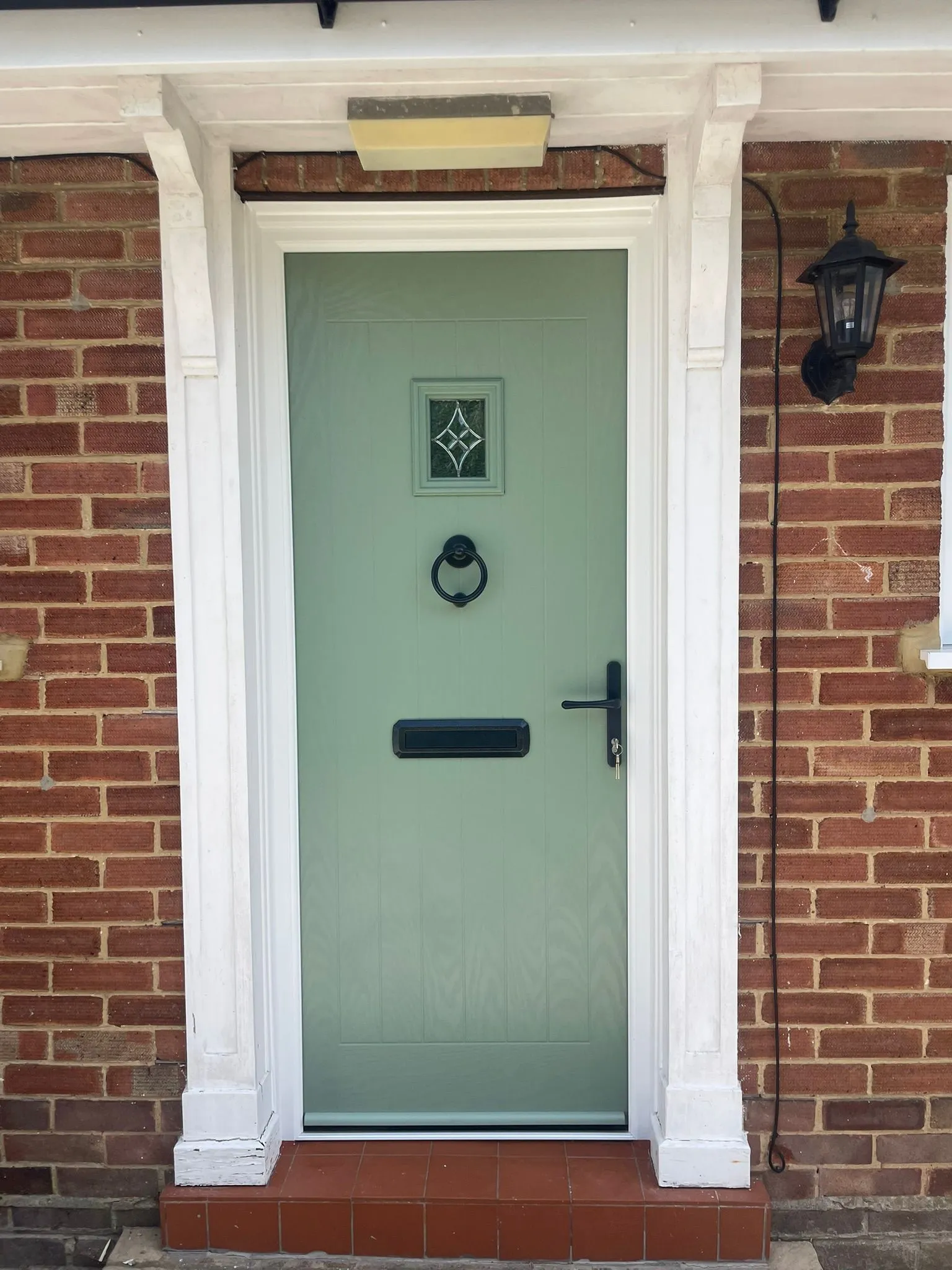 Traditional style pale green composite front door with square glazed panel at top.