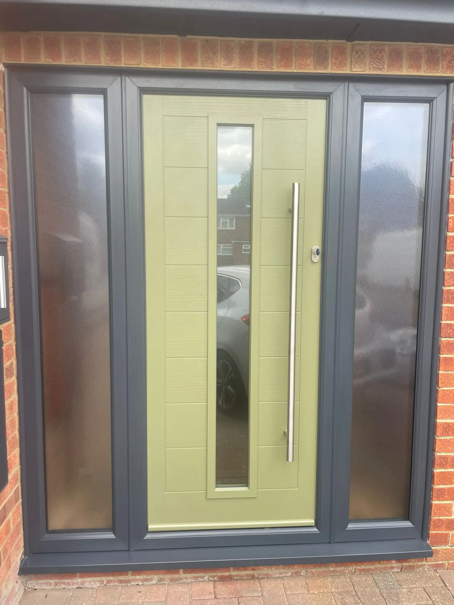 Olive green composite front door with tall chrome handle and frosted side panels.