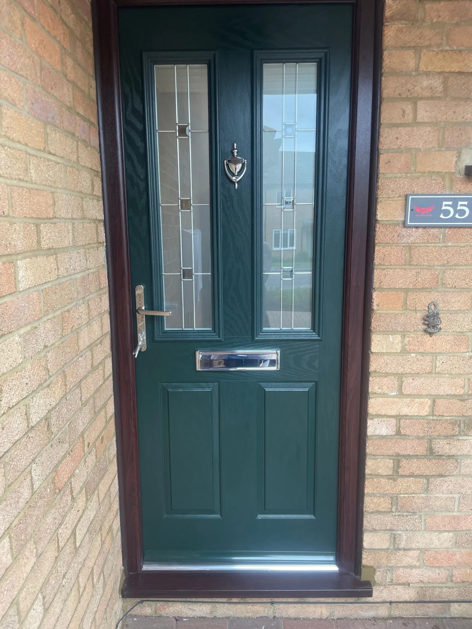 Dark green composite front door with glass inserts and chrome hardware.