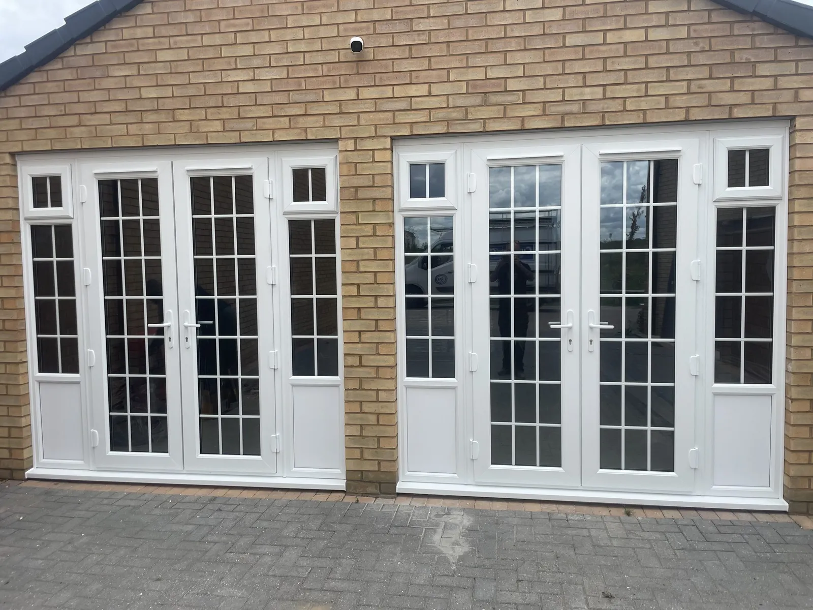 Two pairs of white uPVC French doors with Georgian bars and side lights fitted across the front of a buff brick building.