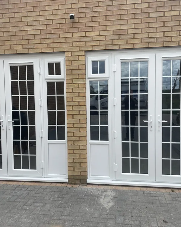 Two pairs of white uPVC French doors with Georgian bars and side lights fitted across the front of a buff brick building.