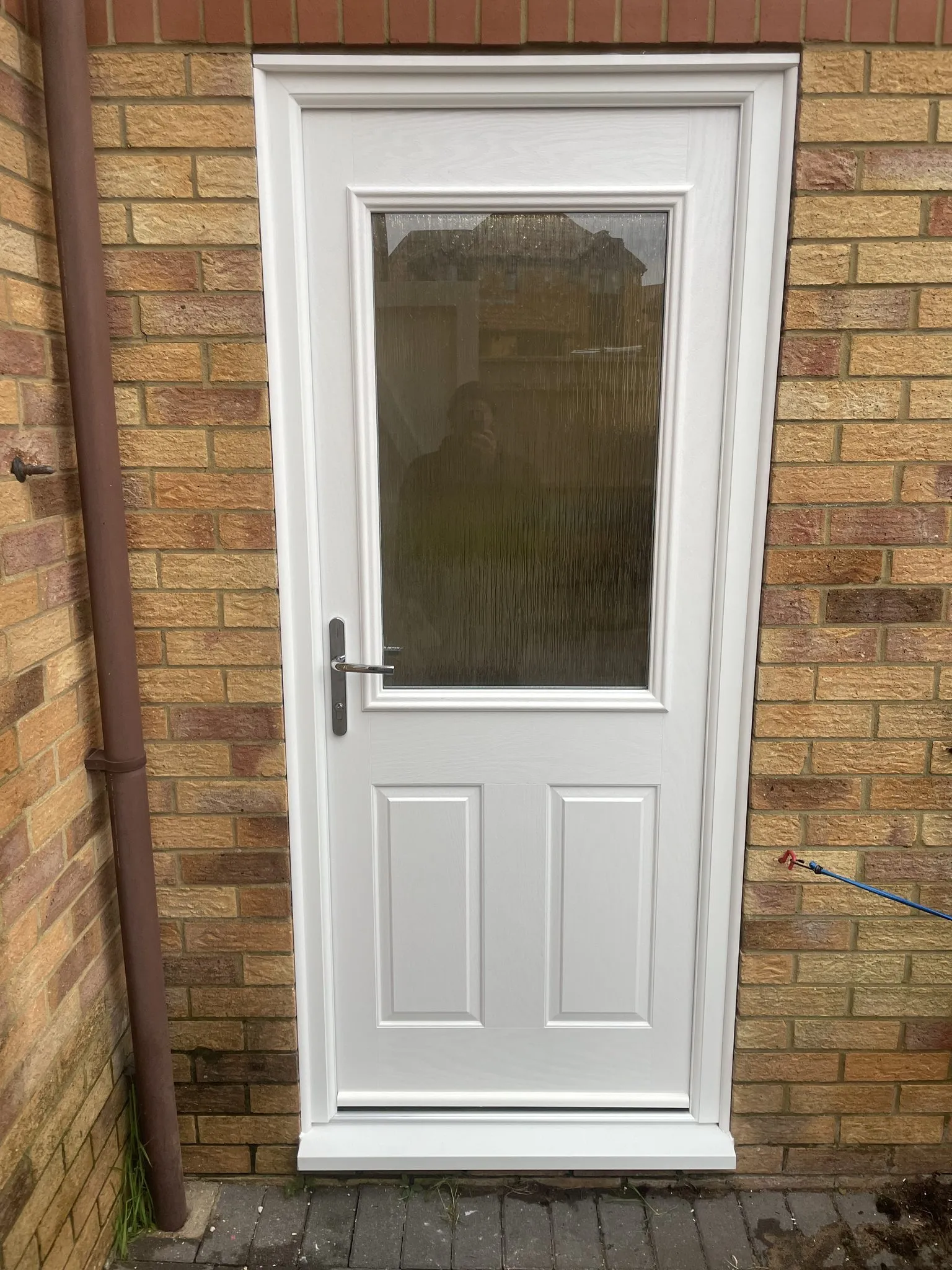 White composite back door with an obscure glazed top panel and two moulded lower panels, fitted in a buff brick wall.