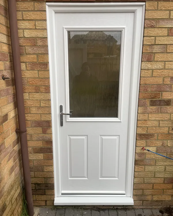 White composite back door with an obscure glazed top panel and two moulded lower panels, fitted in a buff brick wall.