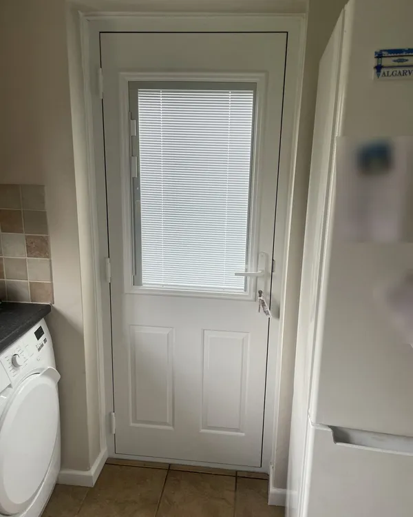 Inside view of a white composite back door with integral blinds sealed within the glass, in a utility room.