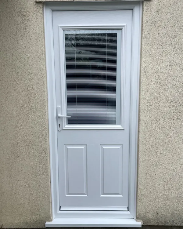 White composite back door with a glazed panel containing integral blinds, fitted in a rendered wall.