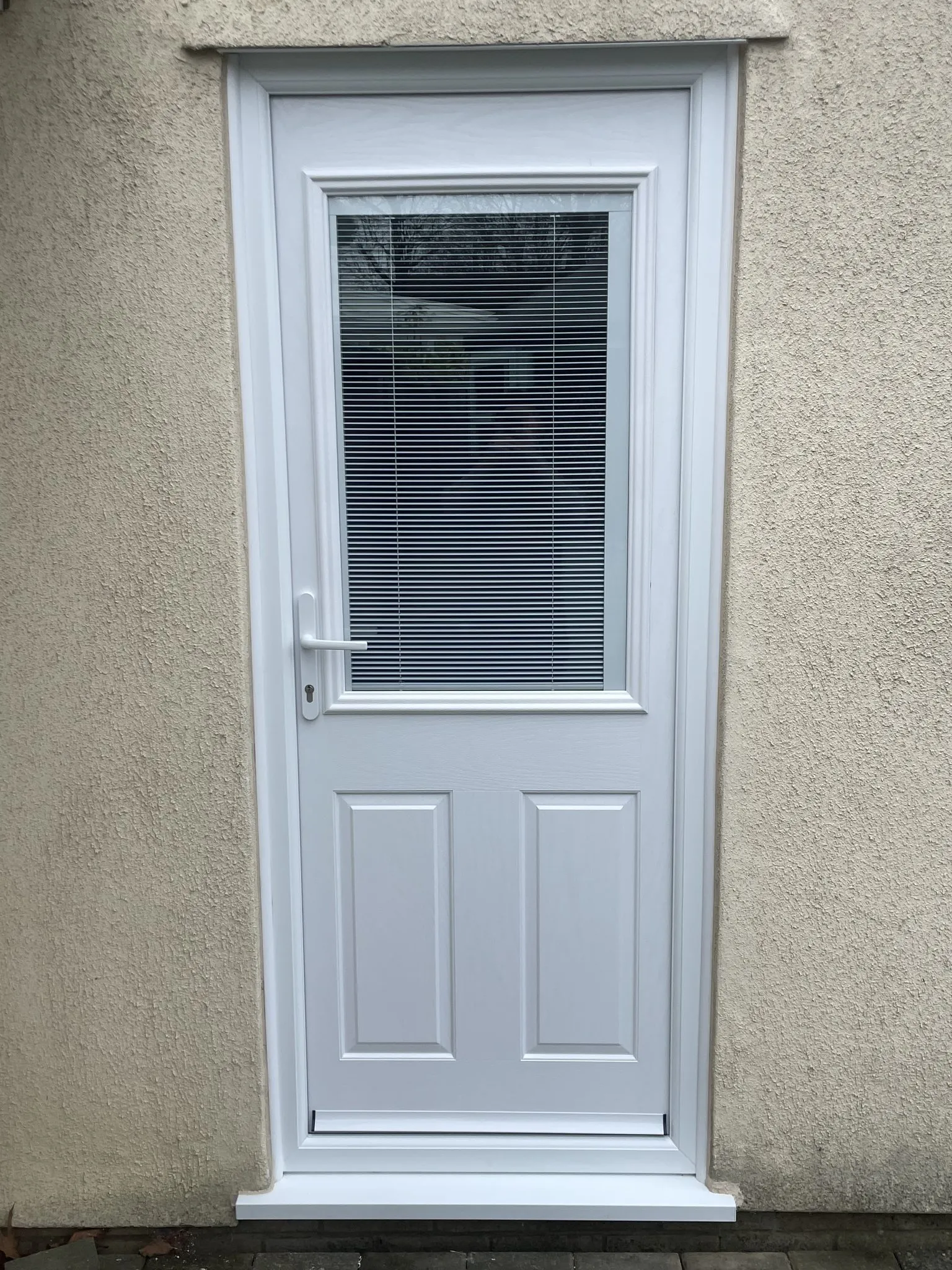 White composite back door with a glazed panel containing integral blinds, fitted in a rendered wall.