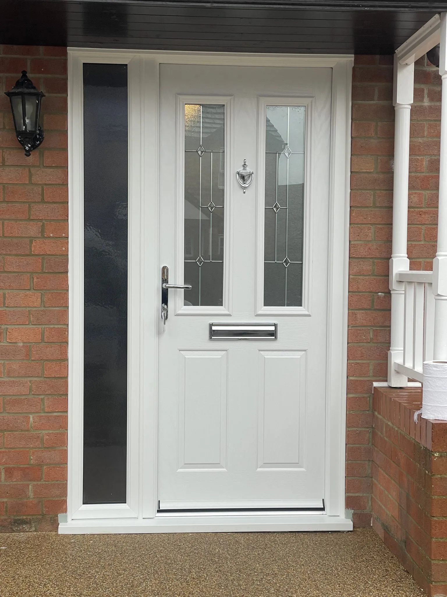 White composite front door with two leaded glass panels and chrome furniture, beside a tall side panel with dark obscure glass.