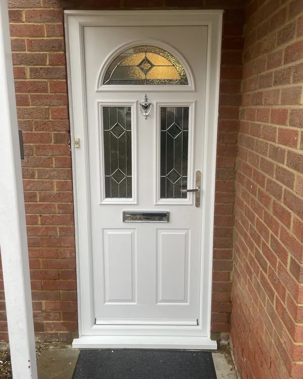 White composite front door with a half-moon leaded glass panel, two glazed panels and chrome furniture, inside a brick porch.