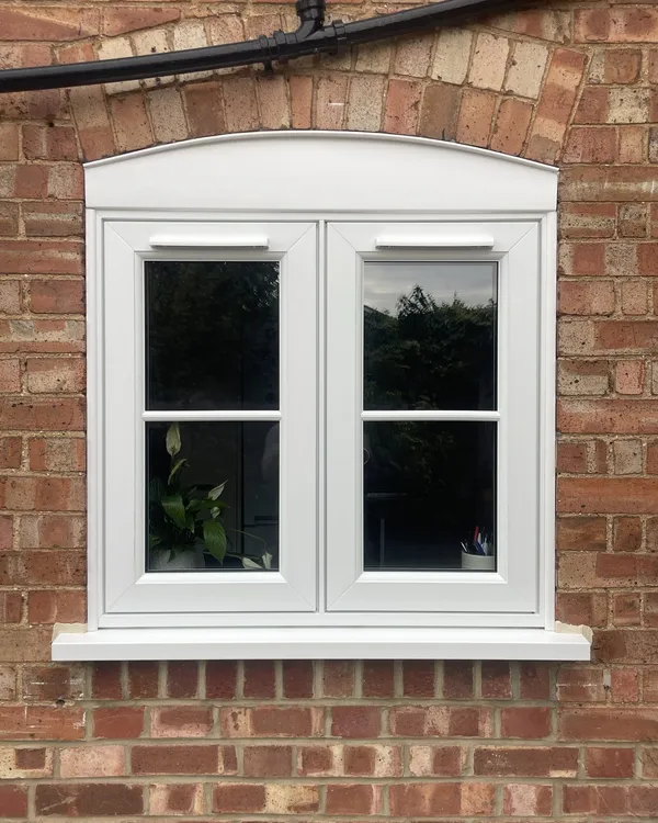 White flush casement window with glazing bars and an arched head, fitted under a brick arch.