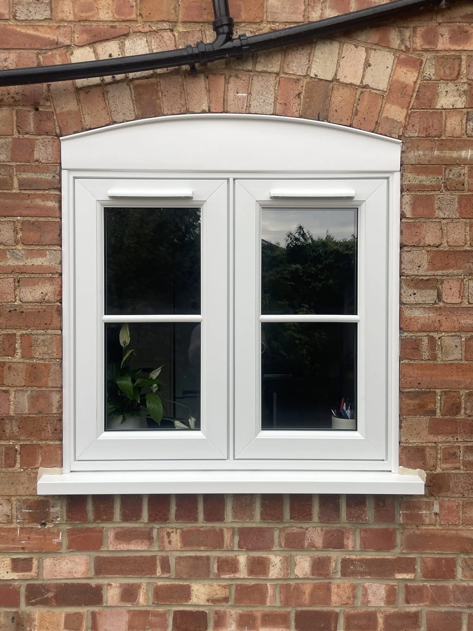 White flush casement window with glazing bars and an arched head, fitted under a brick arch.