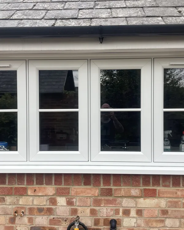 Four-pane white flush casement window with glazing bars, fitted in a red brick wall under a slate roof.