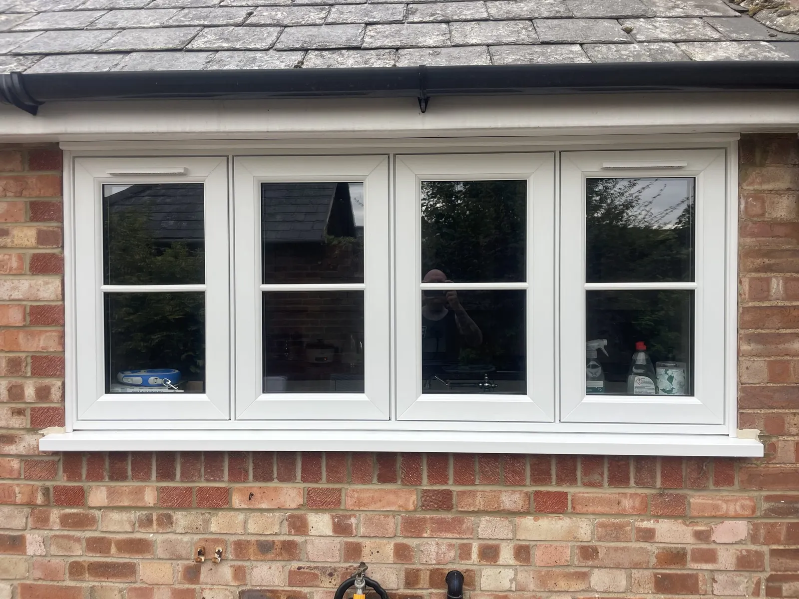 Four-pane white flush casement window with glazing bars, fitted in a red brick wall under a slate roof.