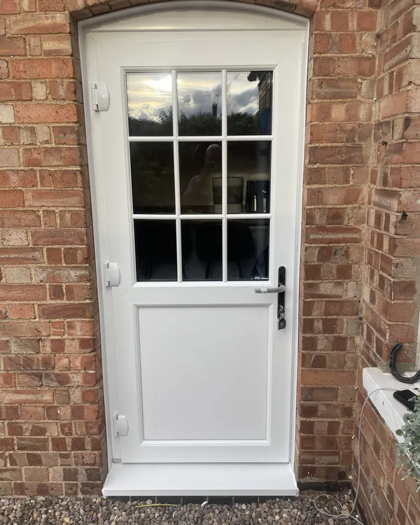 White stable door with a Georgian-barred glazed top half, fitted under a curved brick arch.