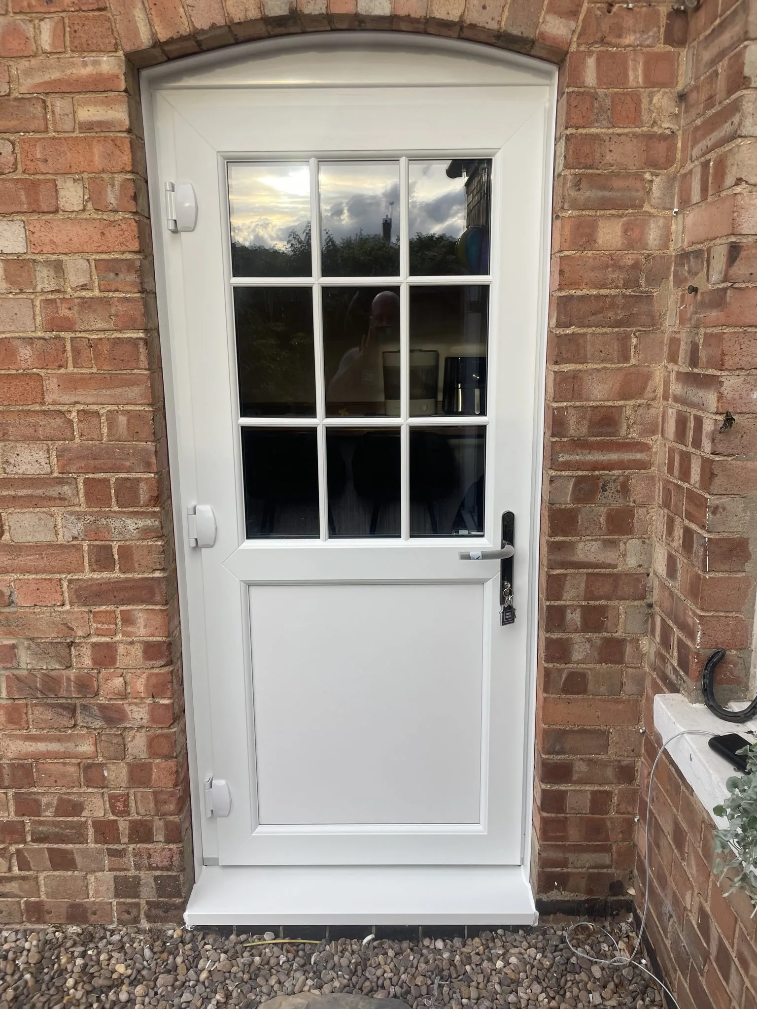 White stable door with a Georgian-barred glazed top half, fitted under a curved brick arch.