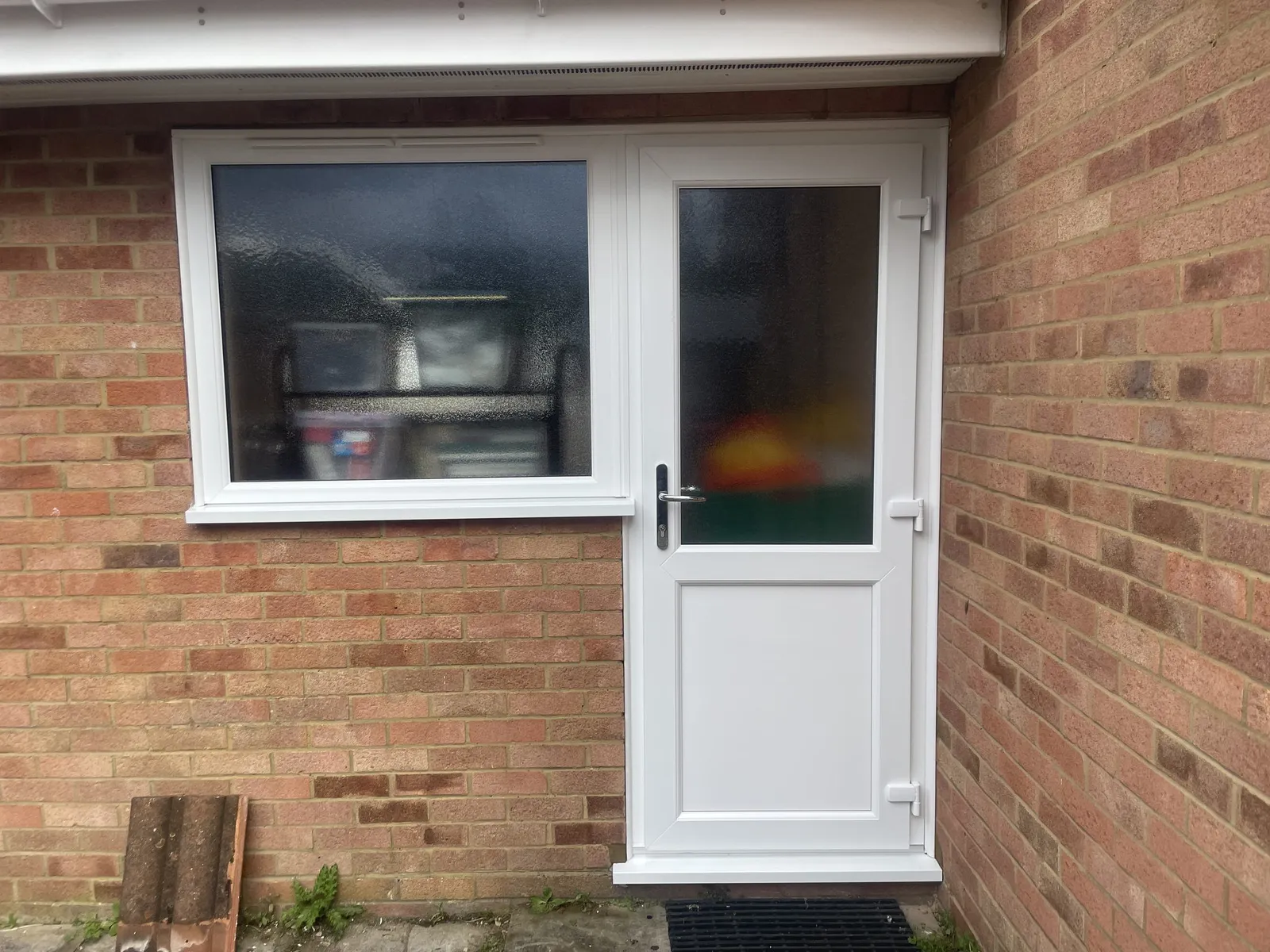 Half-glazed white uPVC back door with obscure glass next to a matching white casement window in a red brick wall.
