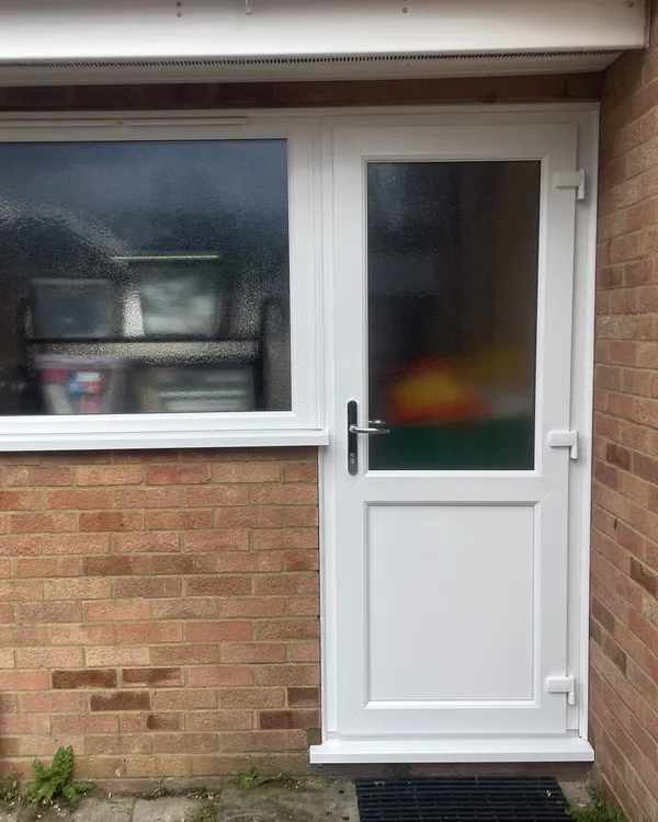 Half-glazed white uPVC back door with obscure glass next to a matching white casement window in a red brick wall.