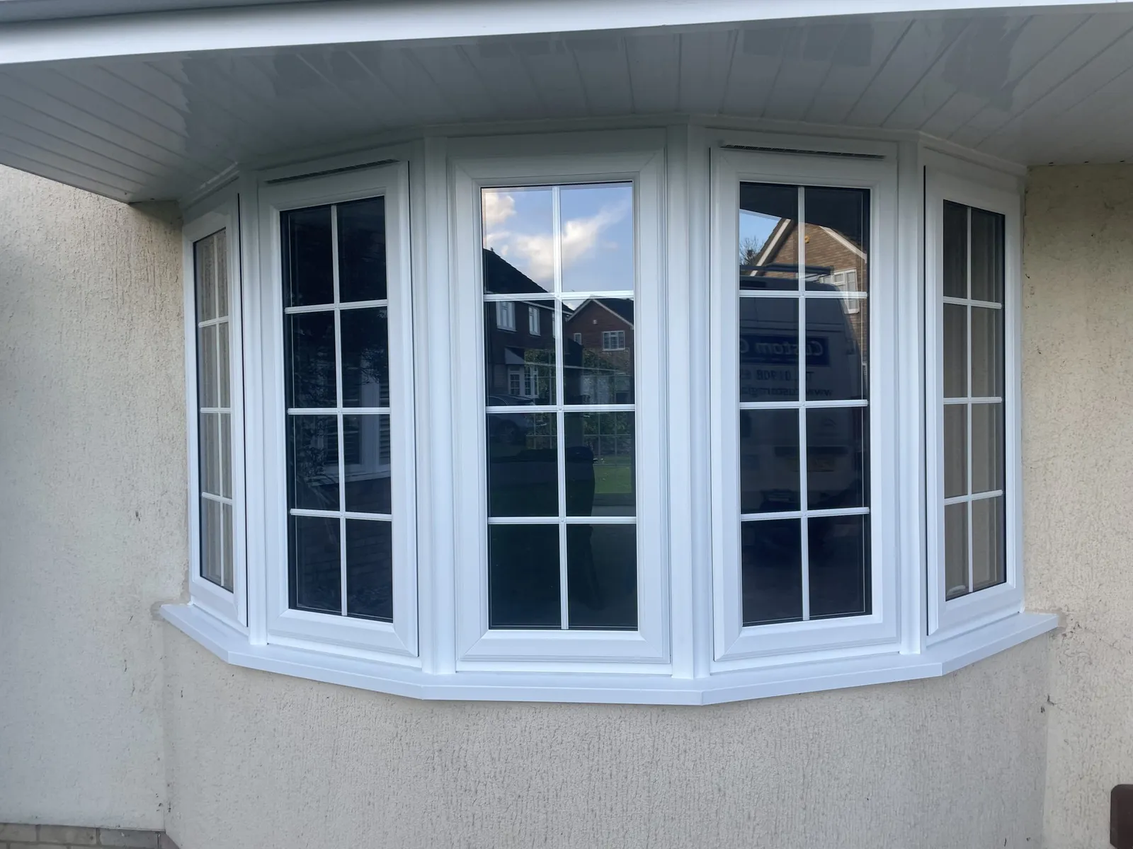 Five-panel white uPVC bay window with Georgian bars fitted in a rendered wall beneath a white soffit.