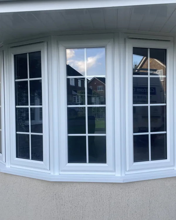 Five-panel white uPVC bay window with Georgian bars fitted in a rendered wall beneath a white soffit.