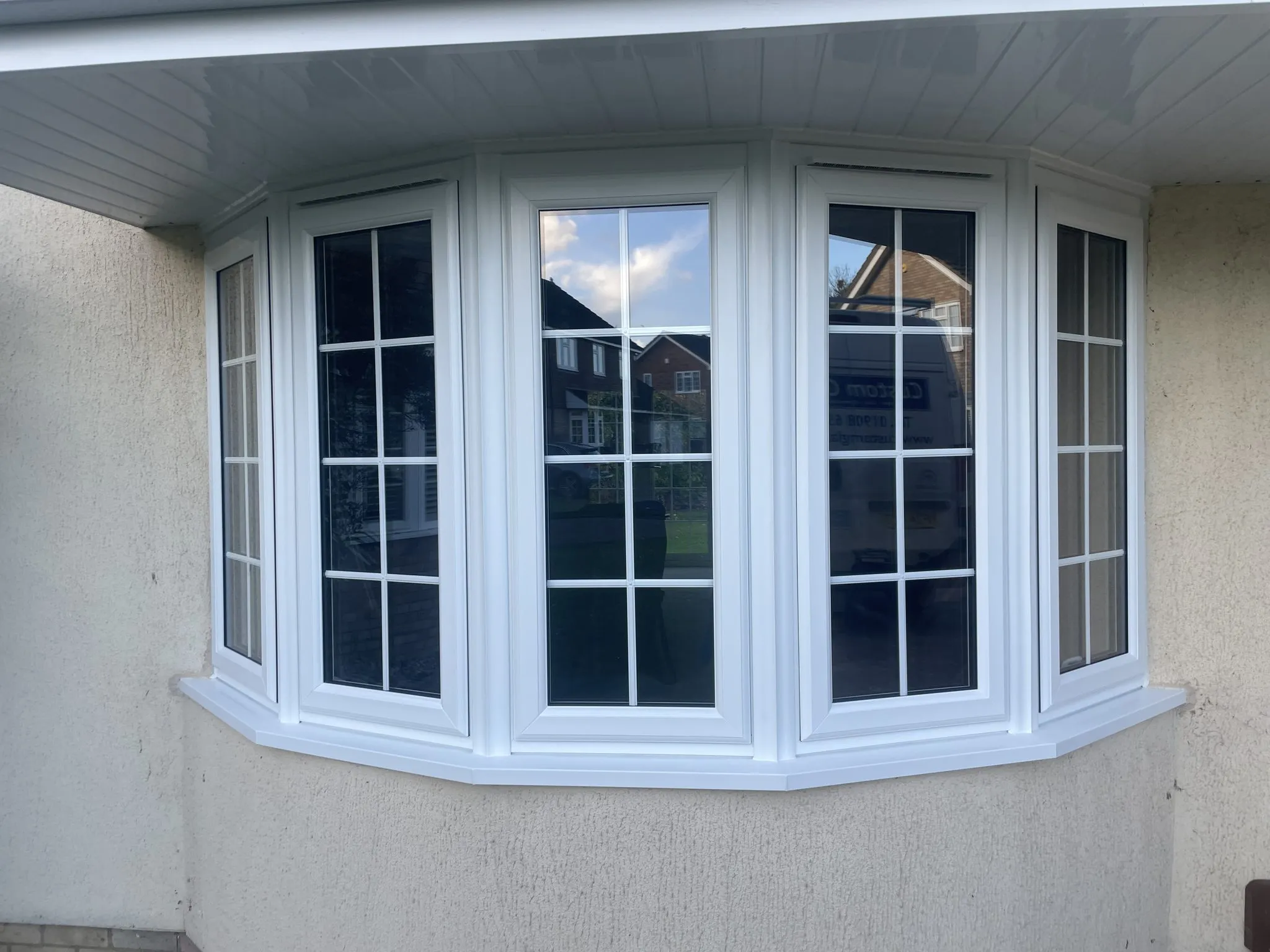 Five-panel white uPVC bay window with Georgian bars fitted in a rendered wall beneath a white soffit.