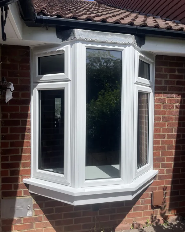 Three-sided white uPVC bay window with top openers fitted on a red brick house beneath a tiled roof.