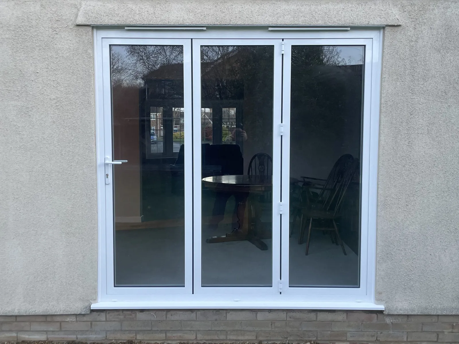Three-panel white uPVC bi-fold doors fitted in a pebbledash rendered wall, looking into a dining room.
