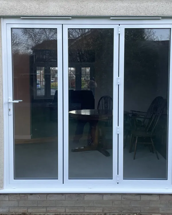 Three-panel white uPVC bi-fold doors fitted in a pebbledash rendered wall, looking into a dining room.