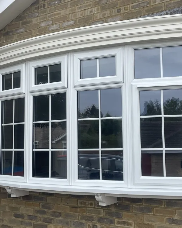 Wide white uPVC bow window with Georgian bars and top openers, under a white canopy on a buff brick house.