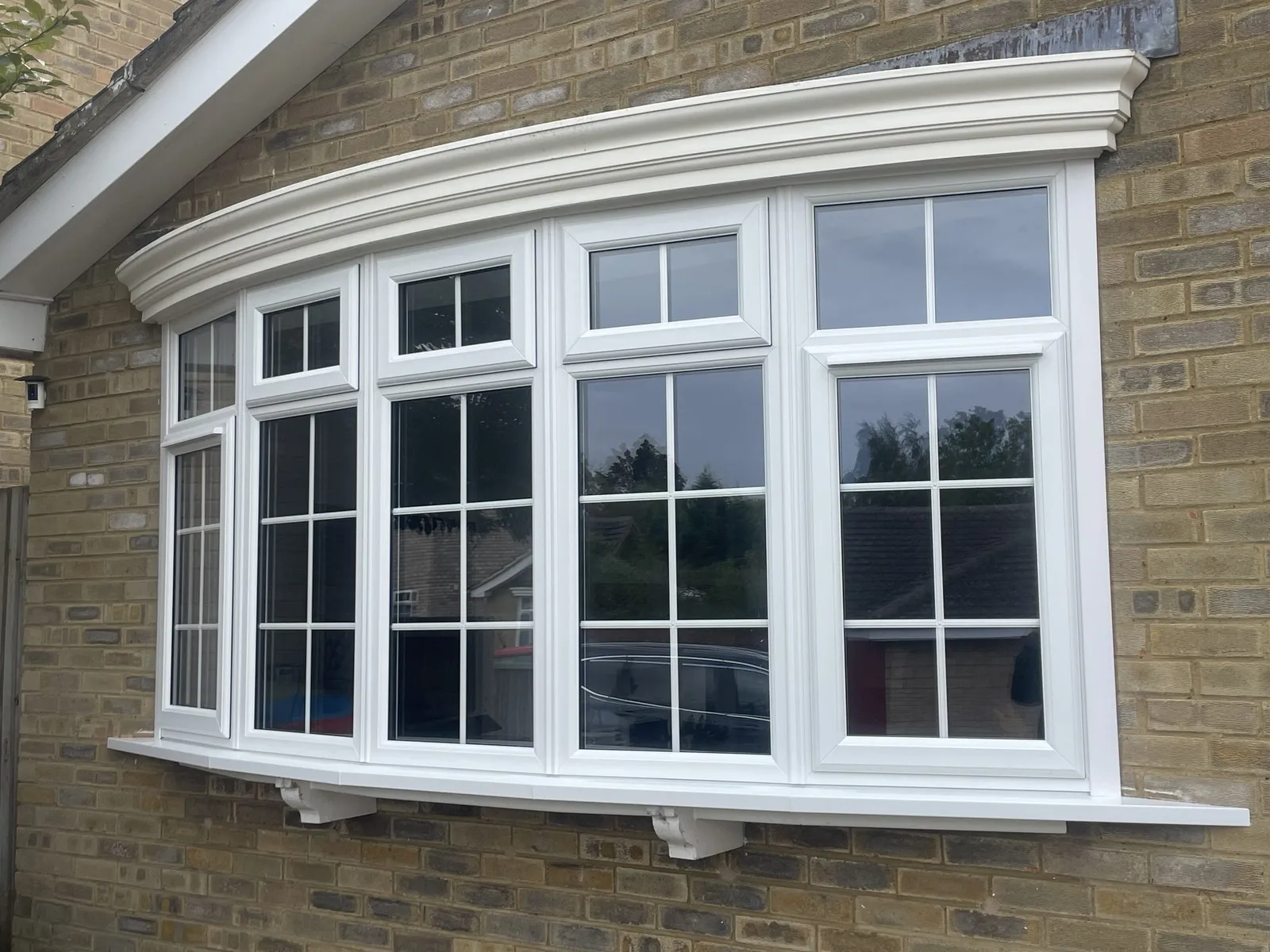 Wide white uPVC bow window with Georgian bars and top openers, under a white canopy on a buff brick house.