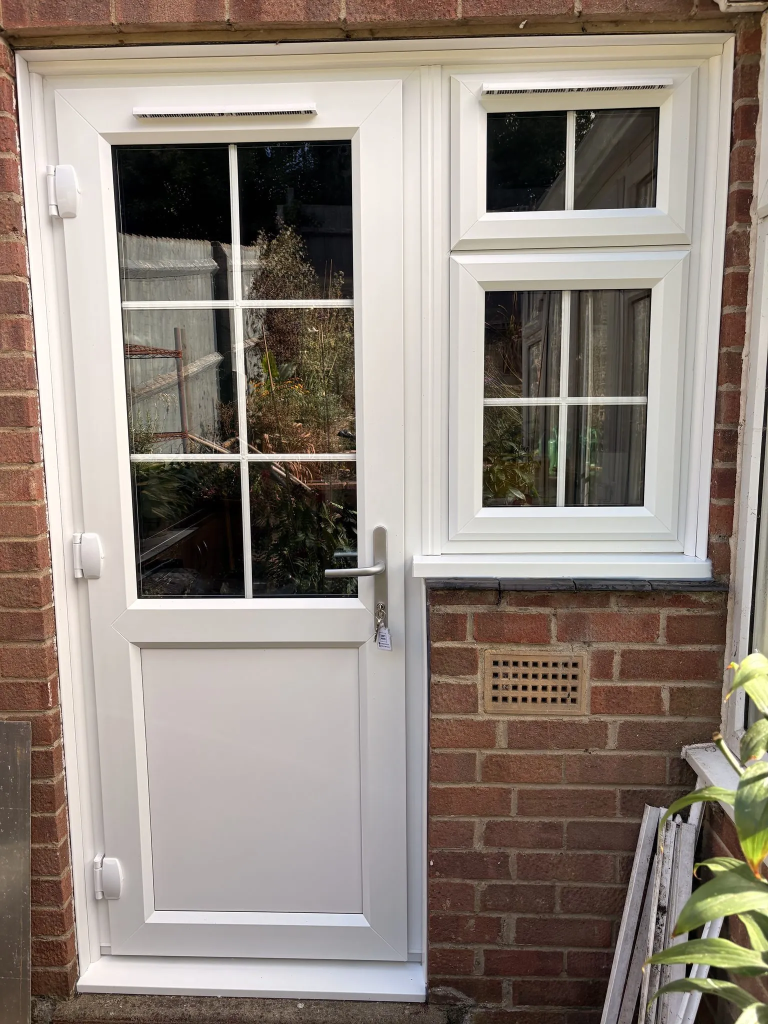 Half-glazed white uPVC back door with Georgian bars, beside a matching white window with a toplight.