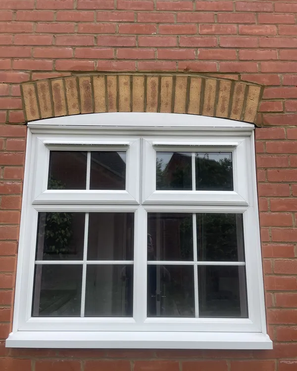 White uPVC double glazed casement window with Georgian bars and top openers, set beneath a curved brick arch in a red brick wall.