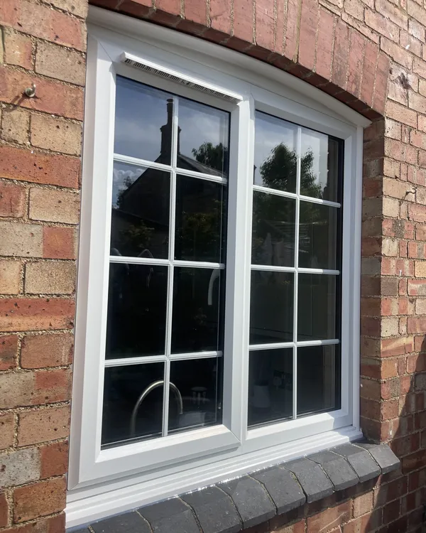 White uPVC casement window with Georgian bars and a curved head, fitted under a brick arch.