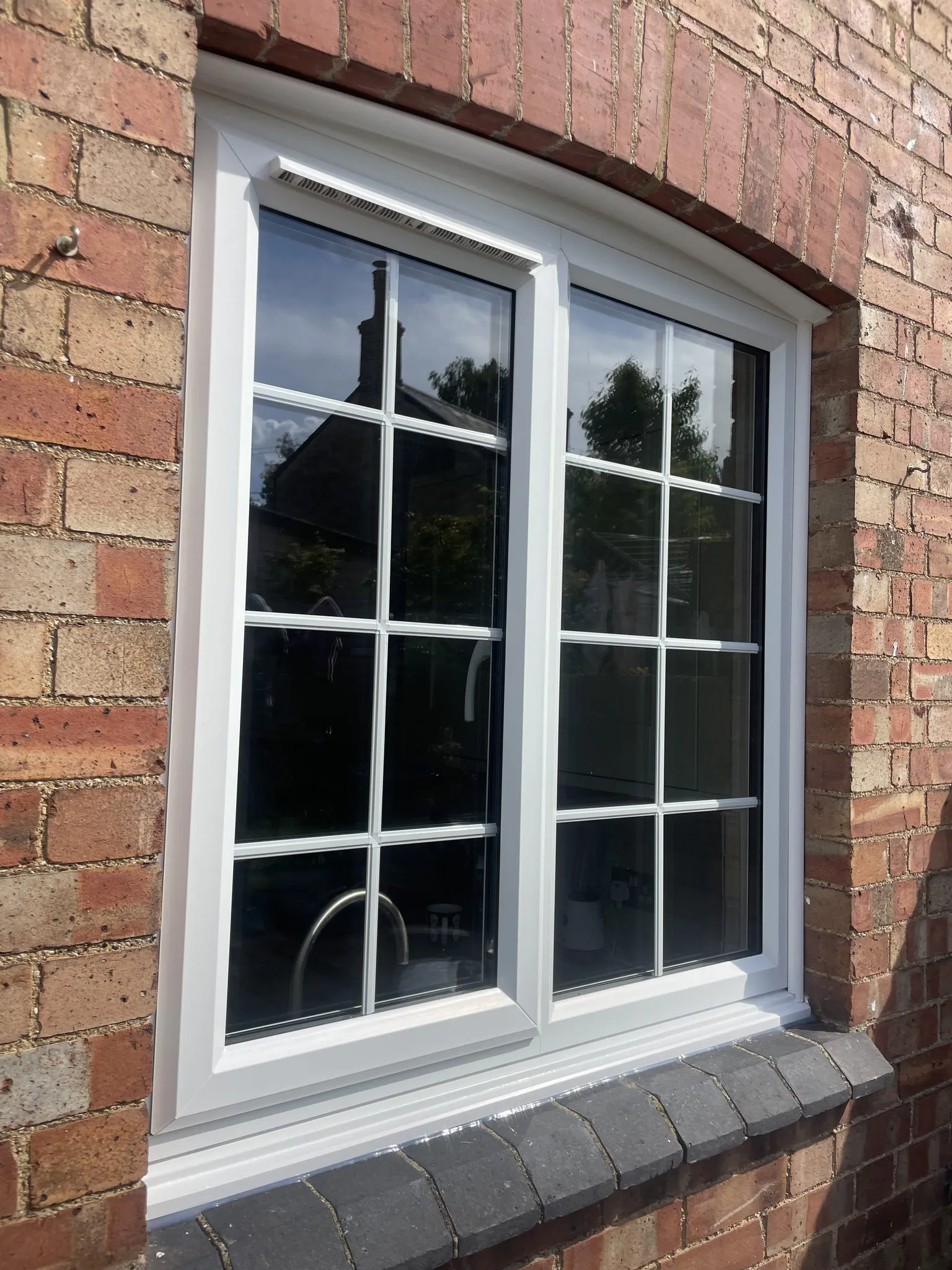 White uPVC casement window with Georgian bars and a curved head, fitted under a brick arch.