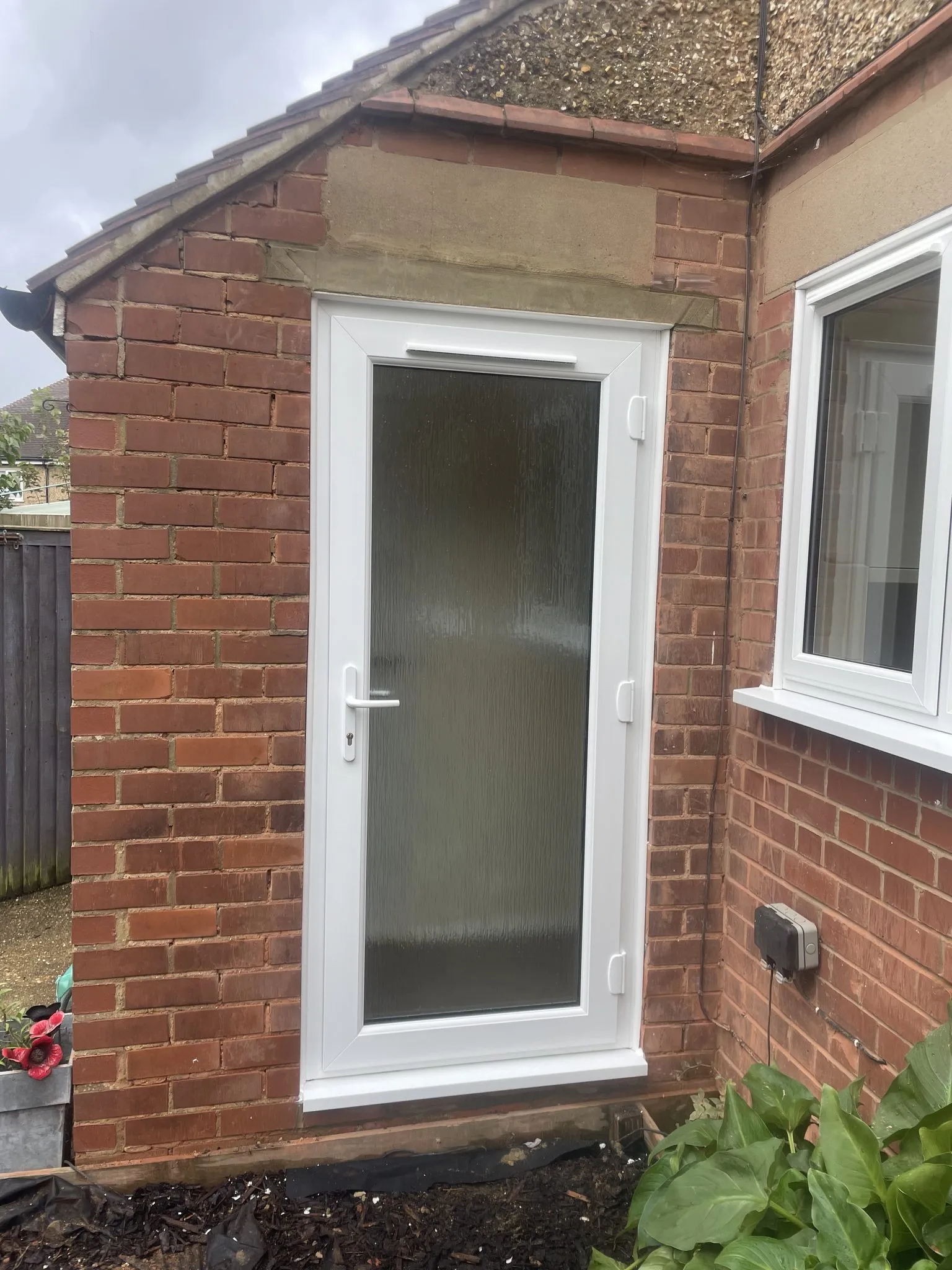 White uPVC back door with a full-height obscure glass panel fitted in a single-storey brick extension, with a white window alongside.