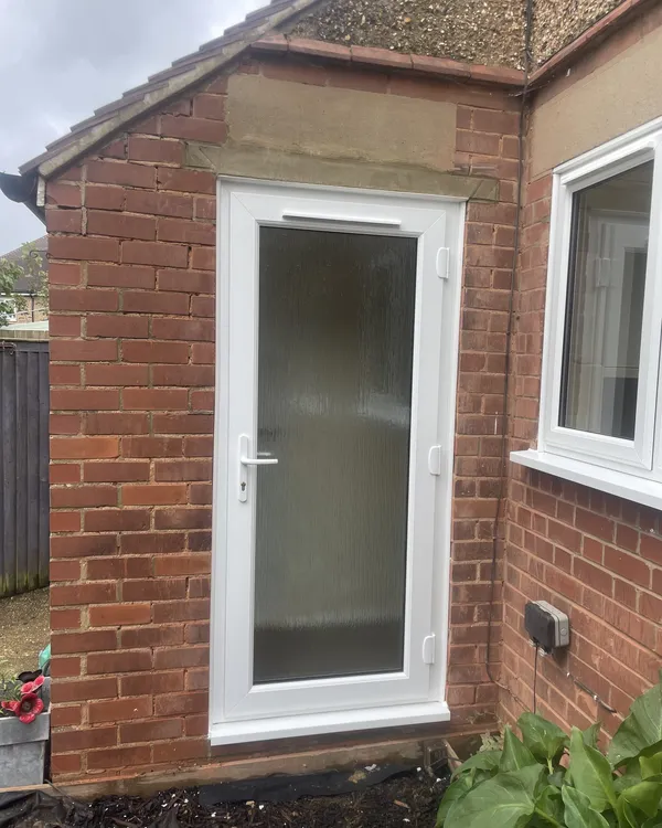 White uPVC back door with a full-height obscure glass panel fitted in a single-storey brick extension, with a white window alongside.