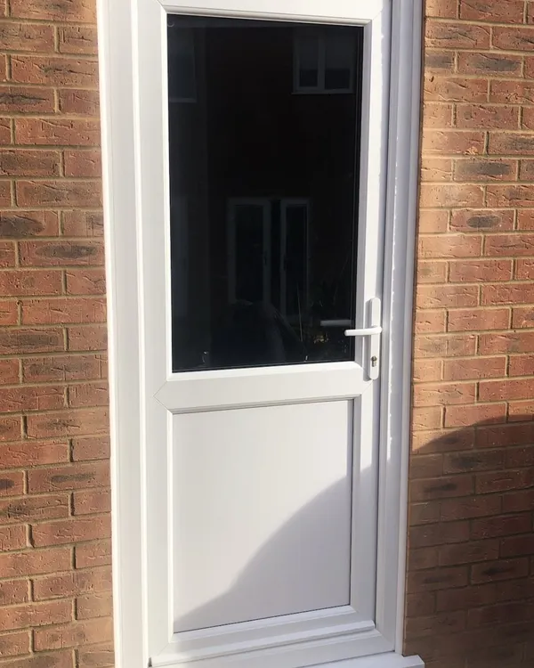 White uPVC back door with a clear glazed top half and a solid lower panel, fitted in a red brick wall.