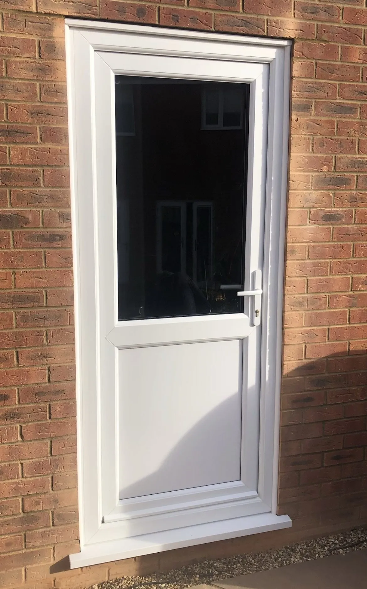 White uPVC back door with a clear glazed top half and a solid lower panel, fitted in a red brick wall.