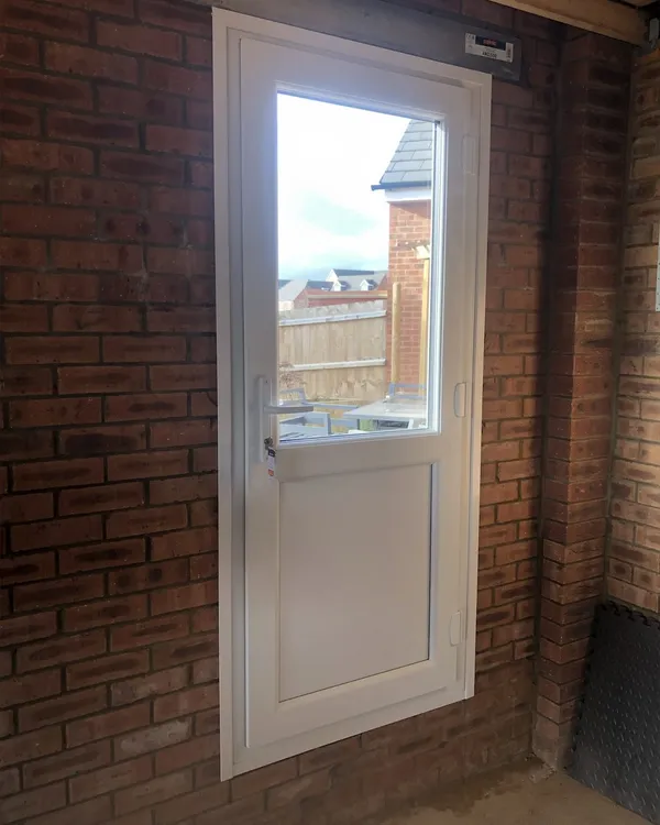 White uPVC half-glazed door fitted in a brick wall under a covered side passage, with a view through to the garden.