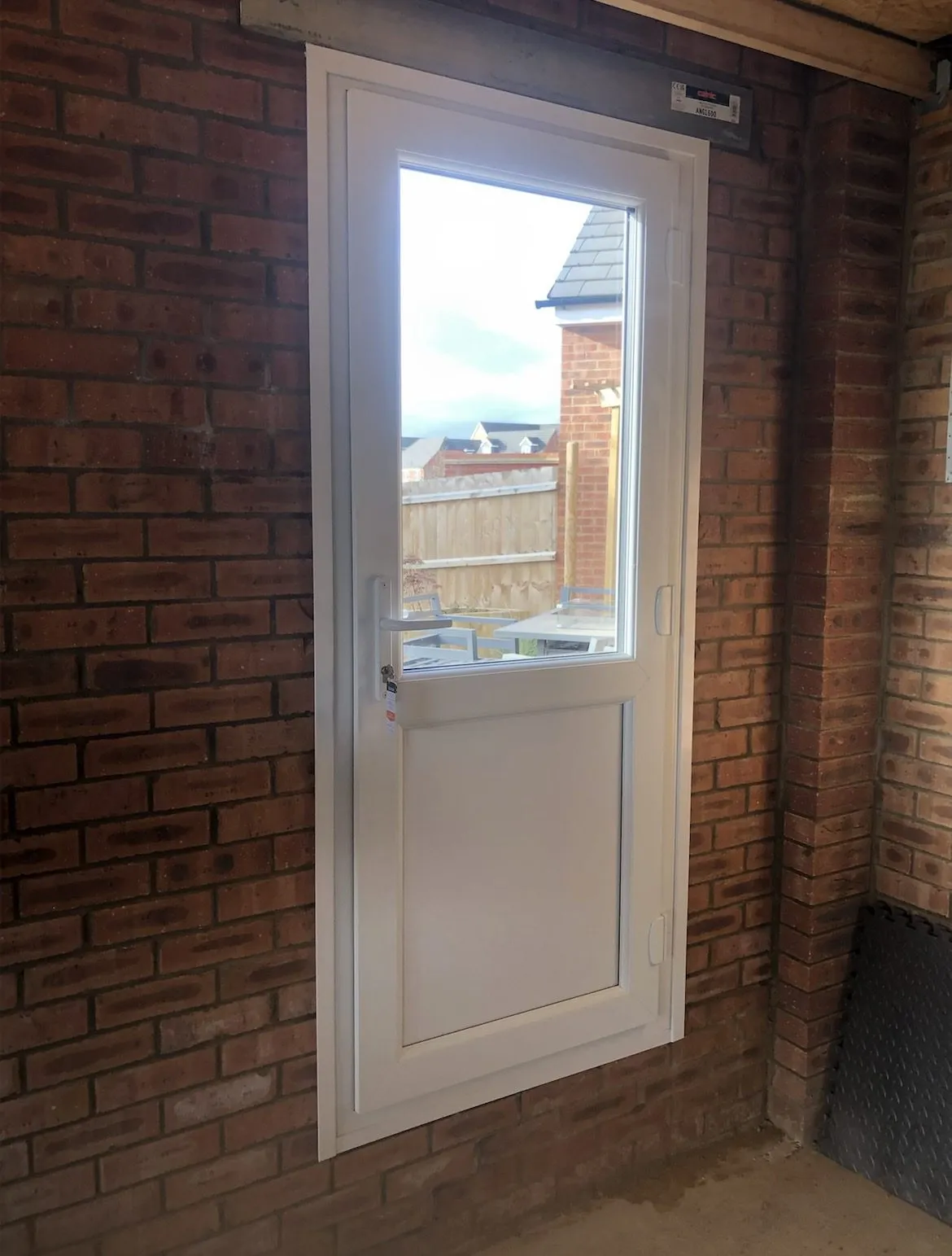White uPVC half-glazed door fitted in a brick wall under a covered side passage, with a view through to the garden.