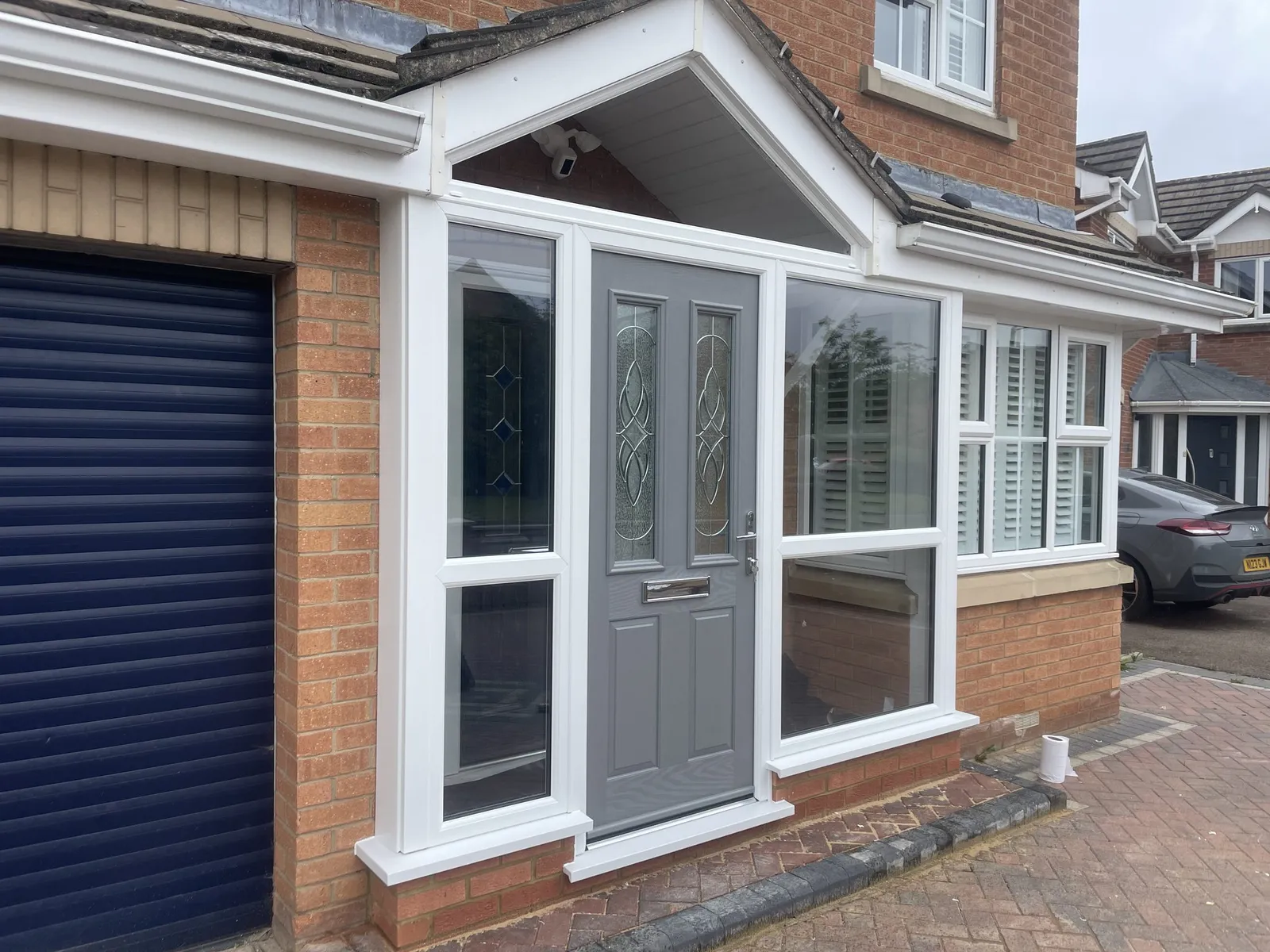 Pitched-roof white uPVC porch with clear glazed sides and a grey composite front door with decorative glass.