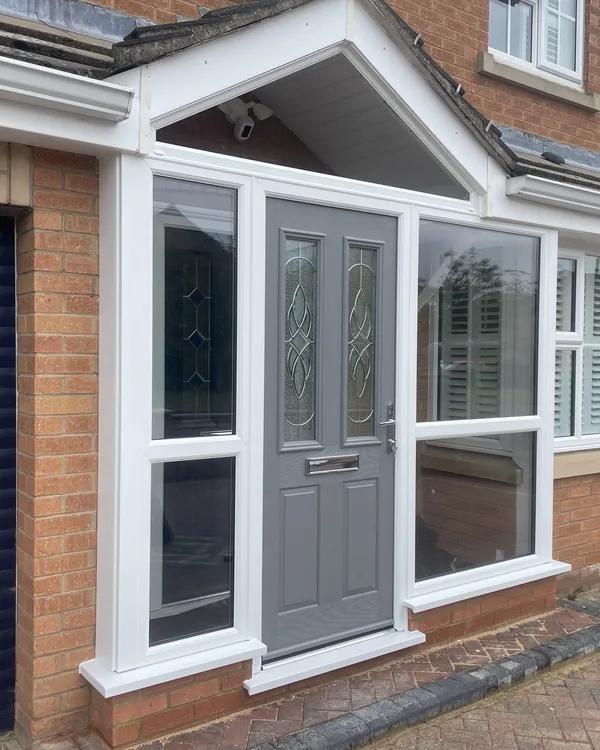 Pitched-roof white uPVC porch with clear glazed sides and a grey composite front door with decorative glass.