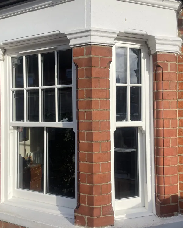 Bay window fitted with white uPVC sliding sash windows with Georgian bars between brick piers on a period house.
