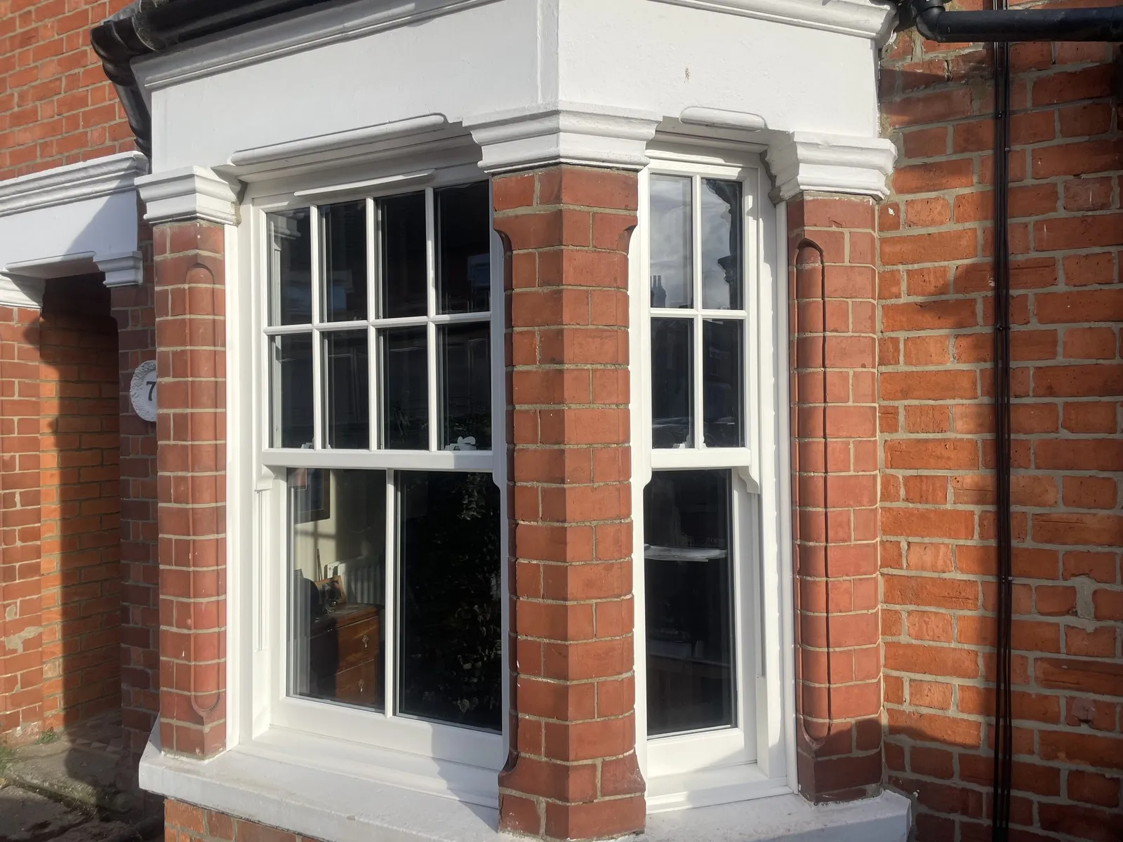 Bay window fitted with white uPVC sliding sash windows with Georgian bars between brick piers on a period house.