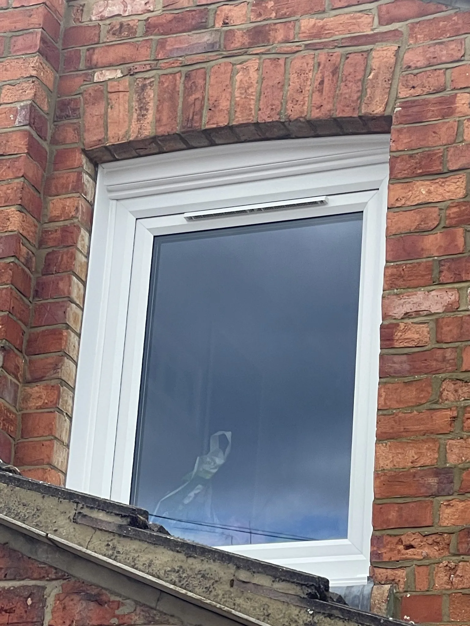 White uPVC window with a trickle vent fitted under a brick arch in an old red brick wall.