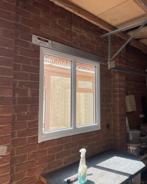 White uPVC window fitted in a red brick wall inside a covered area, with a new steel lintel above.