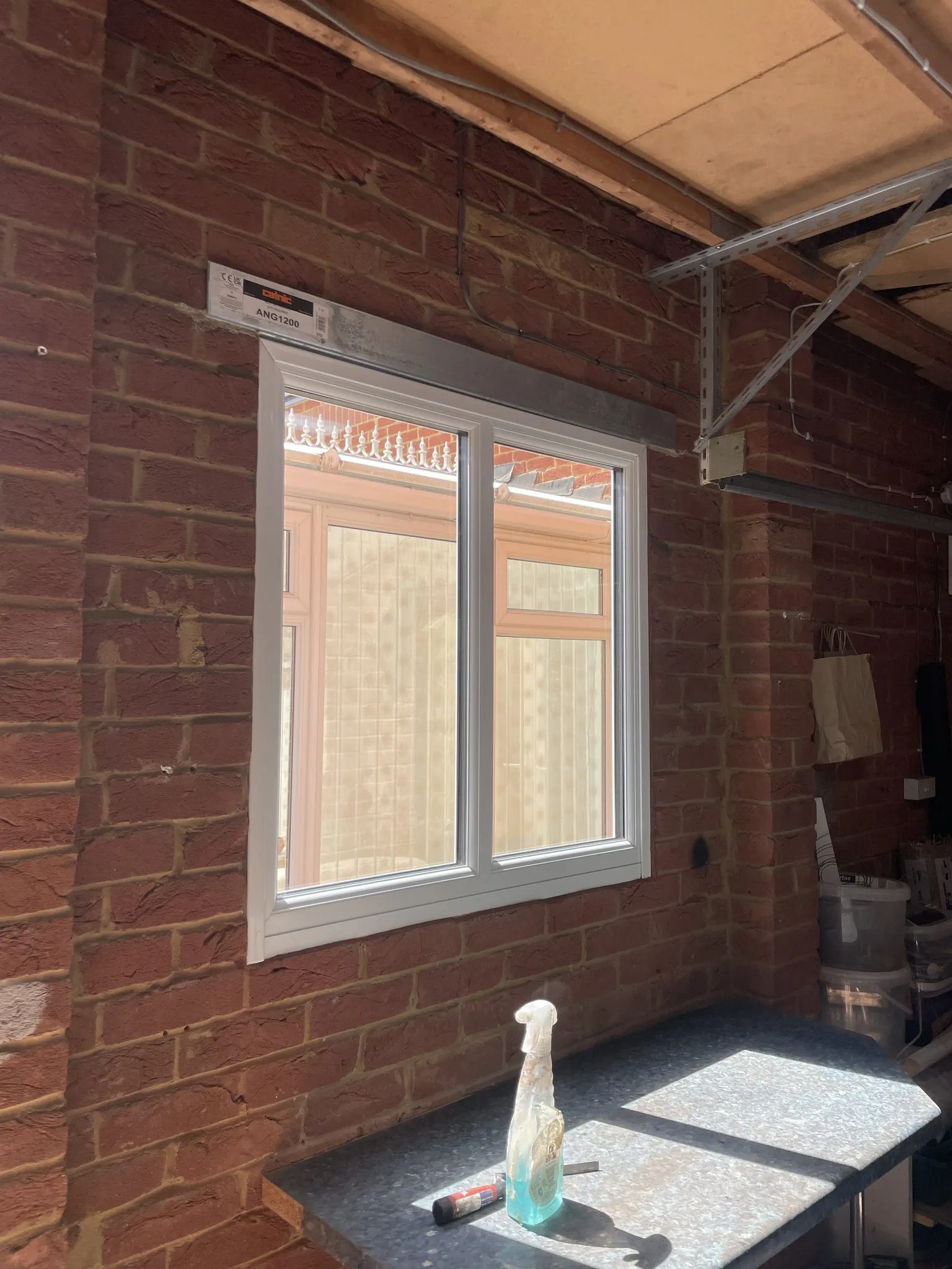 White uPVC window fitted in a red brick wall inside a covered area, with a new steel lintel above.