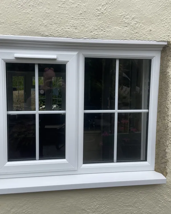 White uPVC casement window with Georgian bars and a deep sill, fitted in a cream rendered wall.
