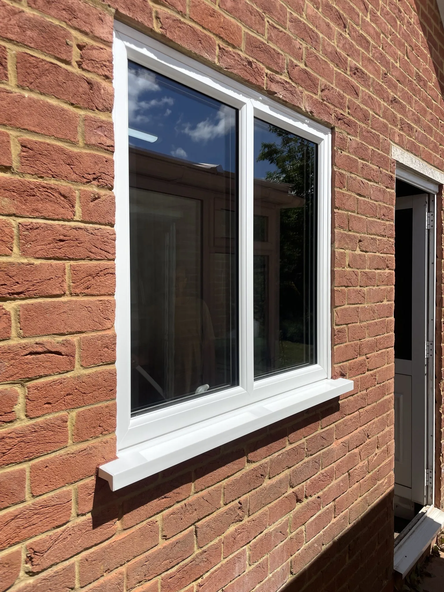 White uPVC casement window with a projecting sill fitted in a red brick wall.